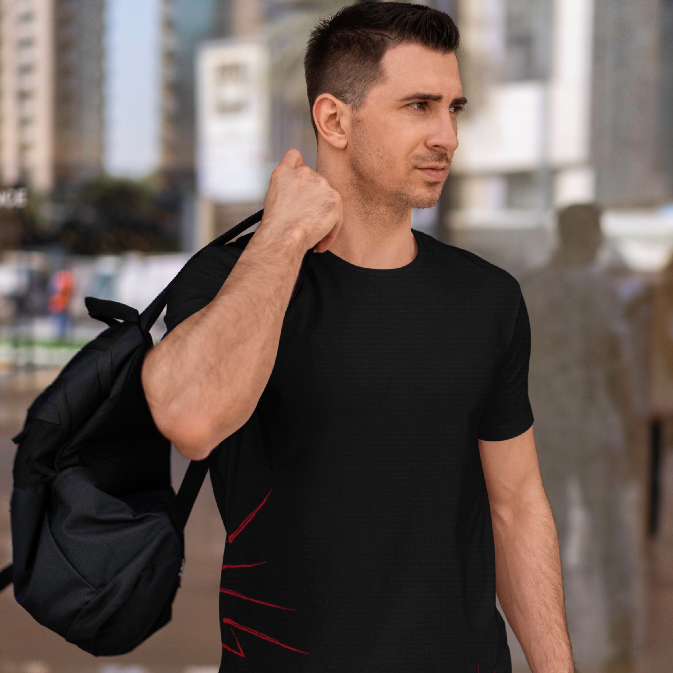 Man wearing a black t-shirt with red designs, holding a black backpack in an urban setting.