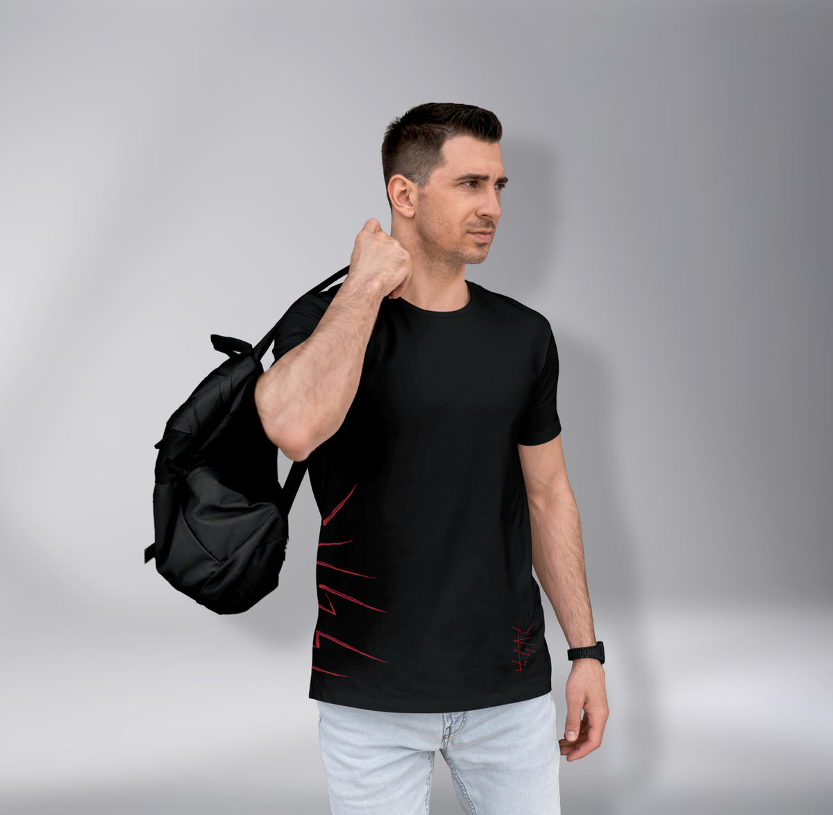 Man wearing a black t-shirt with red designs and holding a black backpack against a gray background