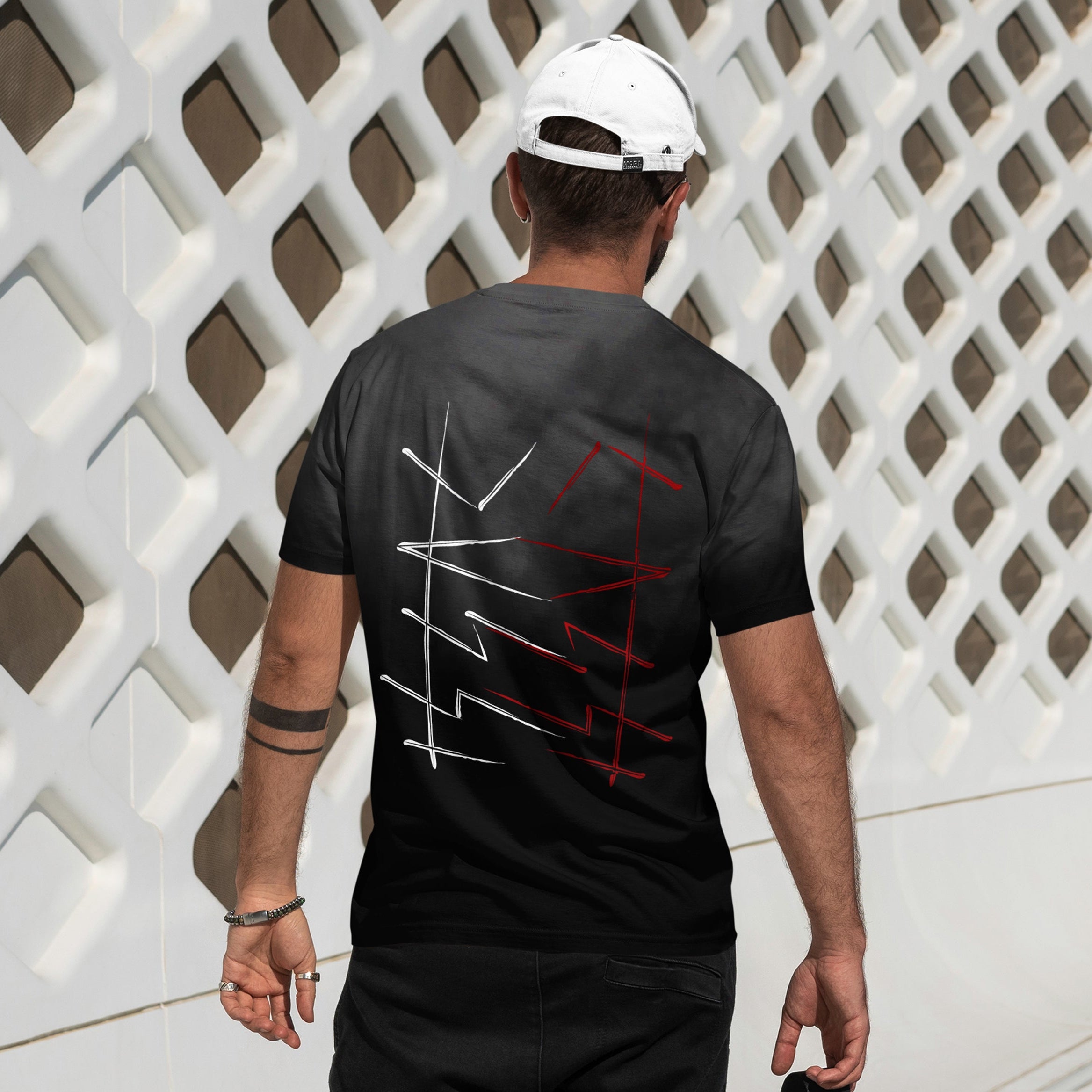 Person wearing a black t-shirt with red and white designs, walking past a white lattice wall.