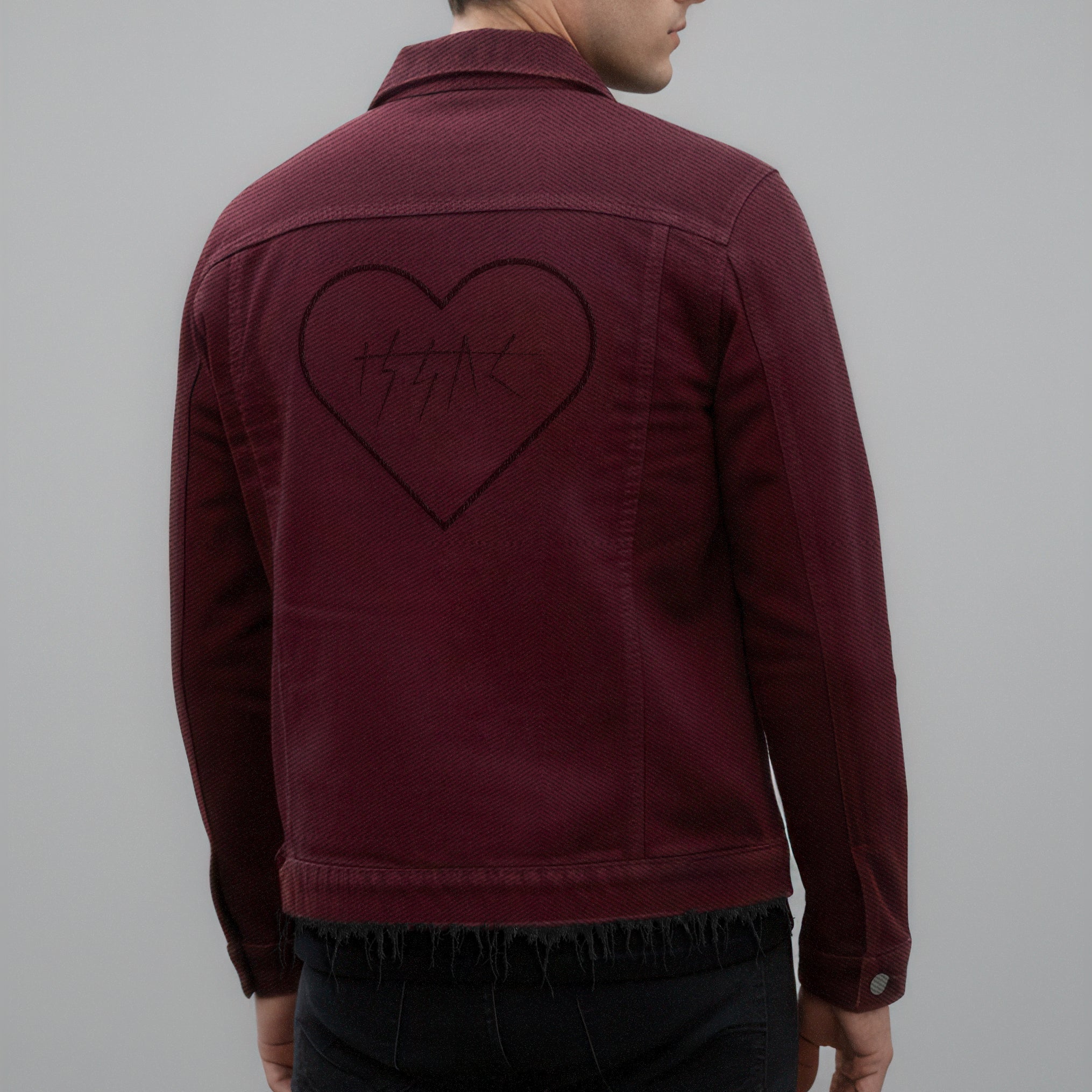 Man wearing a burgundy jacket with a heart design on the back against a gray background